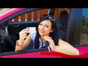 A woman holding up her license and keys in the car.